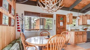 A cozy cabin interior with a wooden dining table, chairs, and a kitchen area.