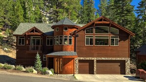 A large, multi-story wooden house with a stone foundation, multiple windows, and a garage.