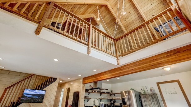 Una amplia cocina estilo loft con vigas de madera, un entrepiso con balcón y un televisor de pantalla plana grande montado en la pared.
