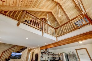 A spacious loft-style kitchen with wooden beams, a mezzanine with a balcony, and a large flat-screen TV mounted on the wall. - Rustic Haven - Hot tub & Pet friendly (South Lake Tahoe)