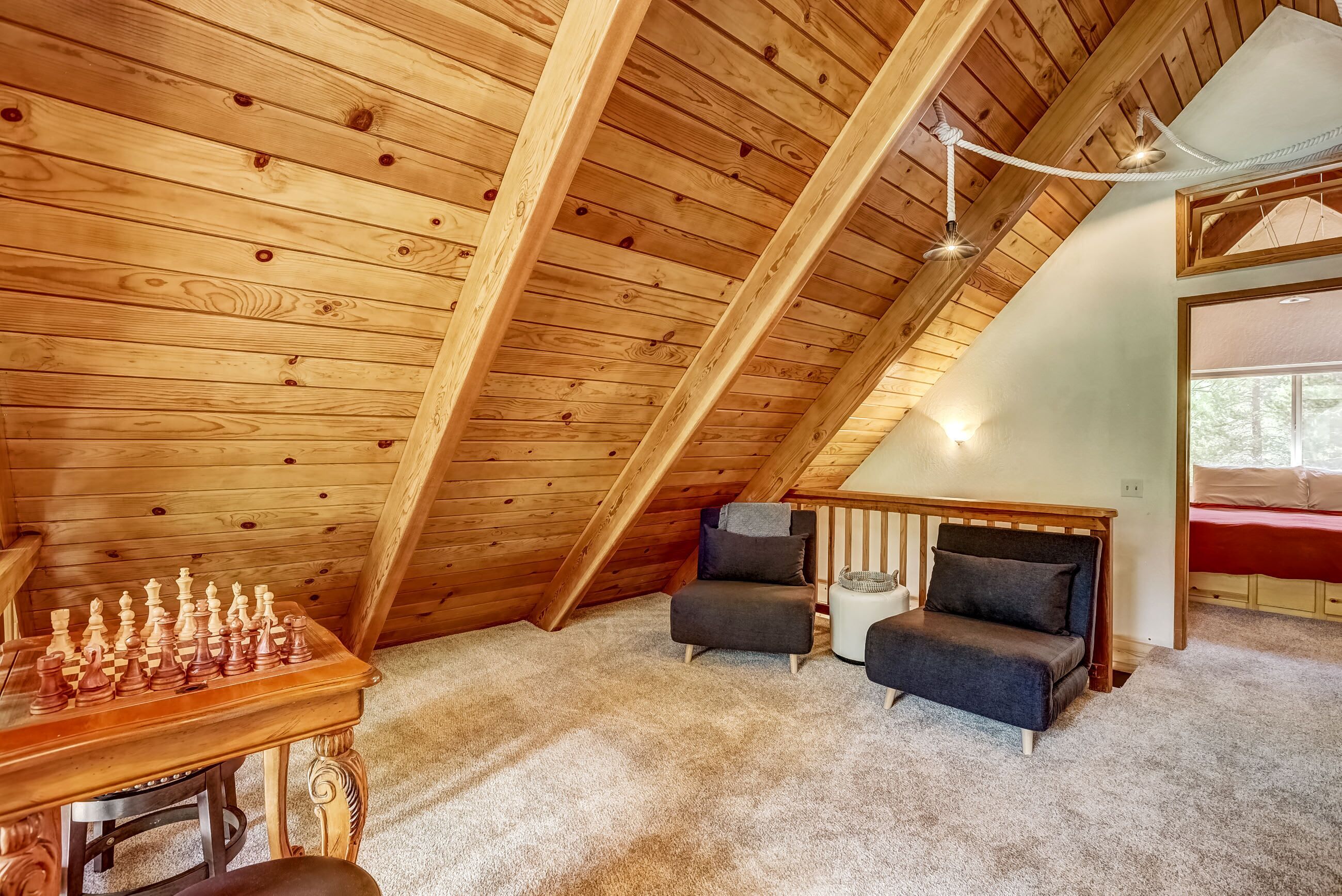 Un acogedor dormitorio en el ático con techo de madera, un tablero de ajedrez, dos sofás y una mesita.