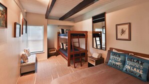 A bedroom with a bunk bed, a desk, a chair, a small bench, and a bed with two decorative pillows.