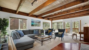 A spacious living room with a grey sectional sofa, a coffee table, and two armchairs. There are large windows and a wooden ceiling. - Hall Court Manor - Hot tub, Pet Friendly, Pool Table! (Stateline)