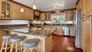 A kitchen with wooden cabinets, granite countertops, stainless steel appliances, and bar stools. - Hall Court Manor - Hot tub, Pet Friendly, Pool Table! (Stateline)