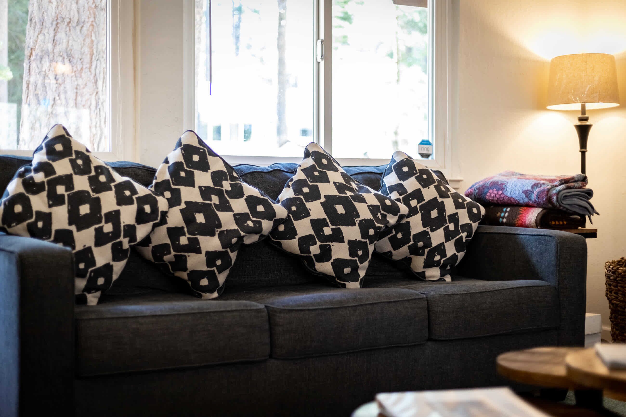 Un canapé gris foncé agrémenté de trois coussins décoratifs à motifs et d’une couverture pliée posée sur un rebord de fenêtre.