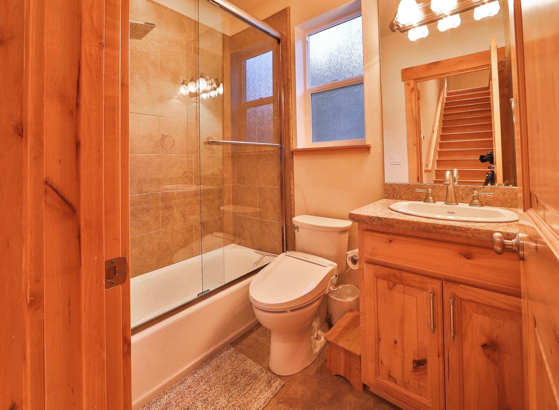 A bathroom with a glass-enclosed shower, a toilet, a bathtub, and wooden cabinets.
