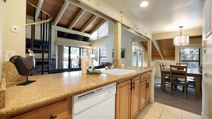 A spacious kitchen with granite countertops, wooden cabinets, and a dishwasher. There is a dining area with a table and chairs, and a large window providing natural light. - Lakeland Sandy Beach Retreat | Private Escape (South Lake Tahoe)