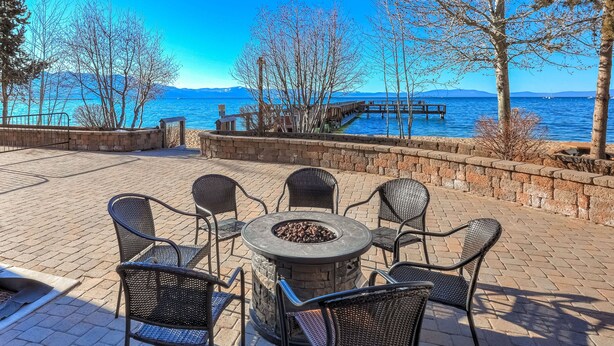 An outdoor seating area with a fire pit and chairs, overlooking a body of water with a dock and mountains in the background. - Lakeland Sandy Beach Retreat | Private Escape (South Lake Tahoe)