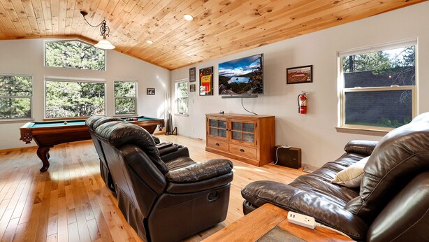 A spacious living room with a pool table, leather recliners, and a wooden cabinet.