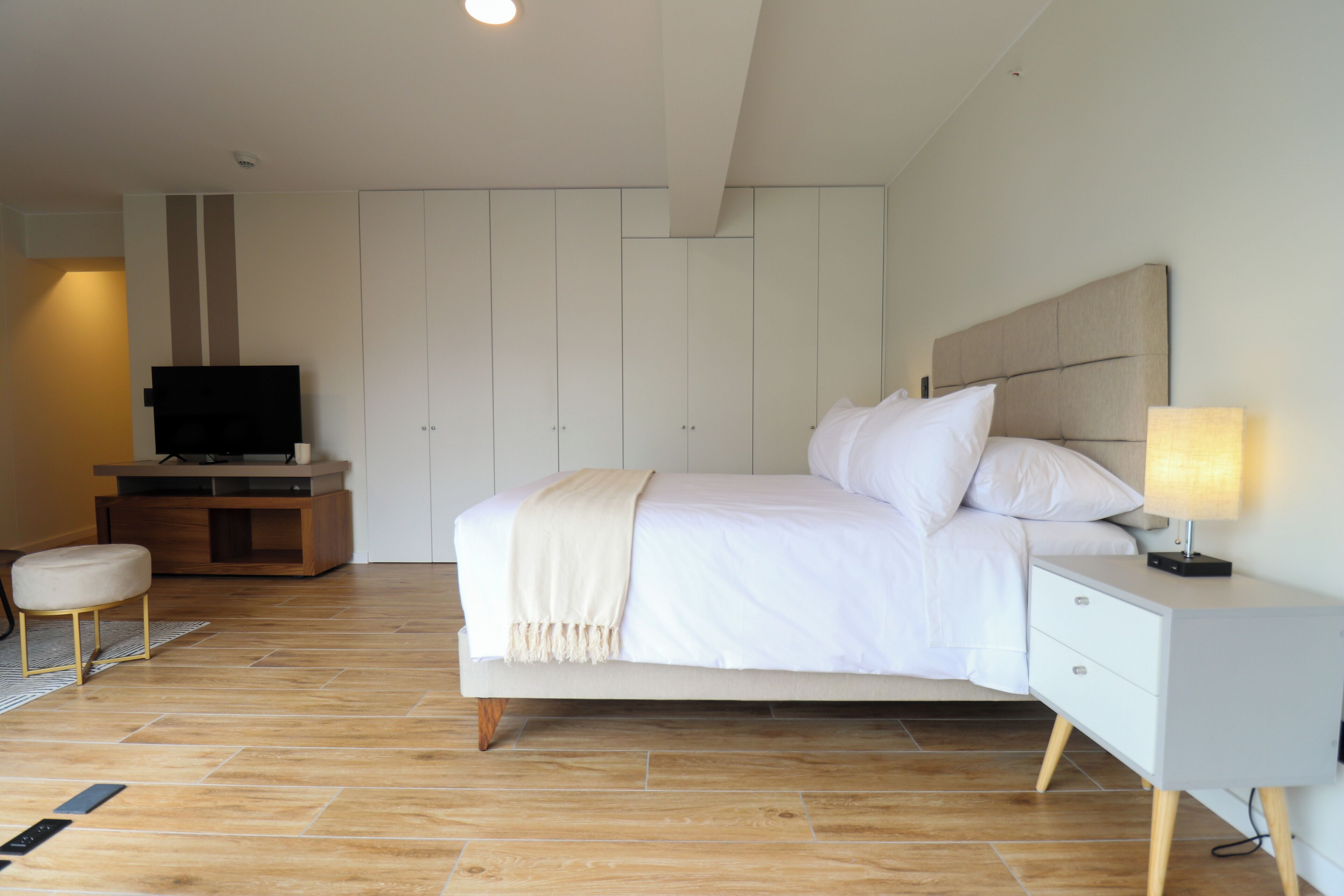 Ein modernes Schlafzimmer mit Bett, Nachttisch, Lampe, Fernseher und Kleiderschrank.