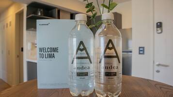 Two water bottles with labels on a wooden table, a welcome sign, and a plant in the background.