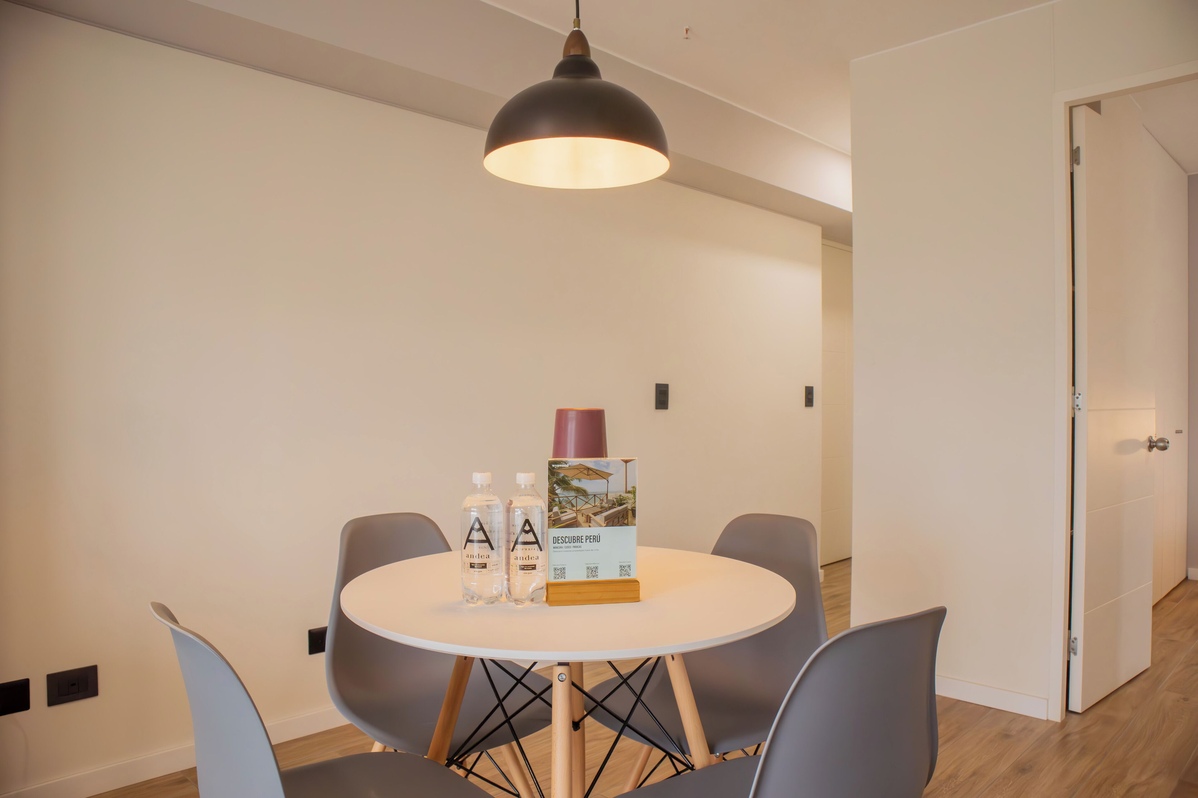 A modern dining area with a round table, grey chairs, a pendant light, and a brochure on the table.