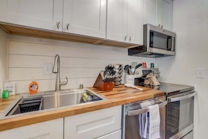 A modern kitchen with a stainless steel sink, wooden countertop, microwave, oven, and cabinets.
