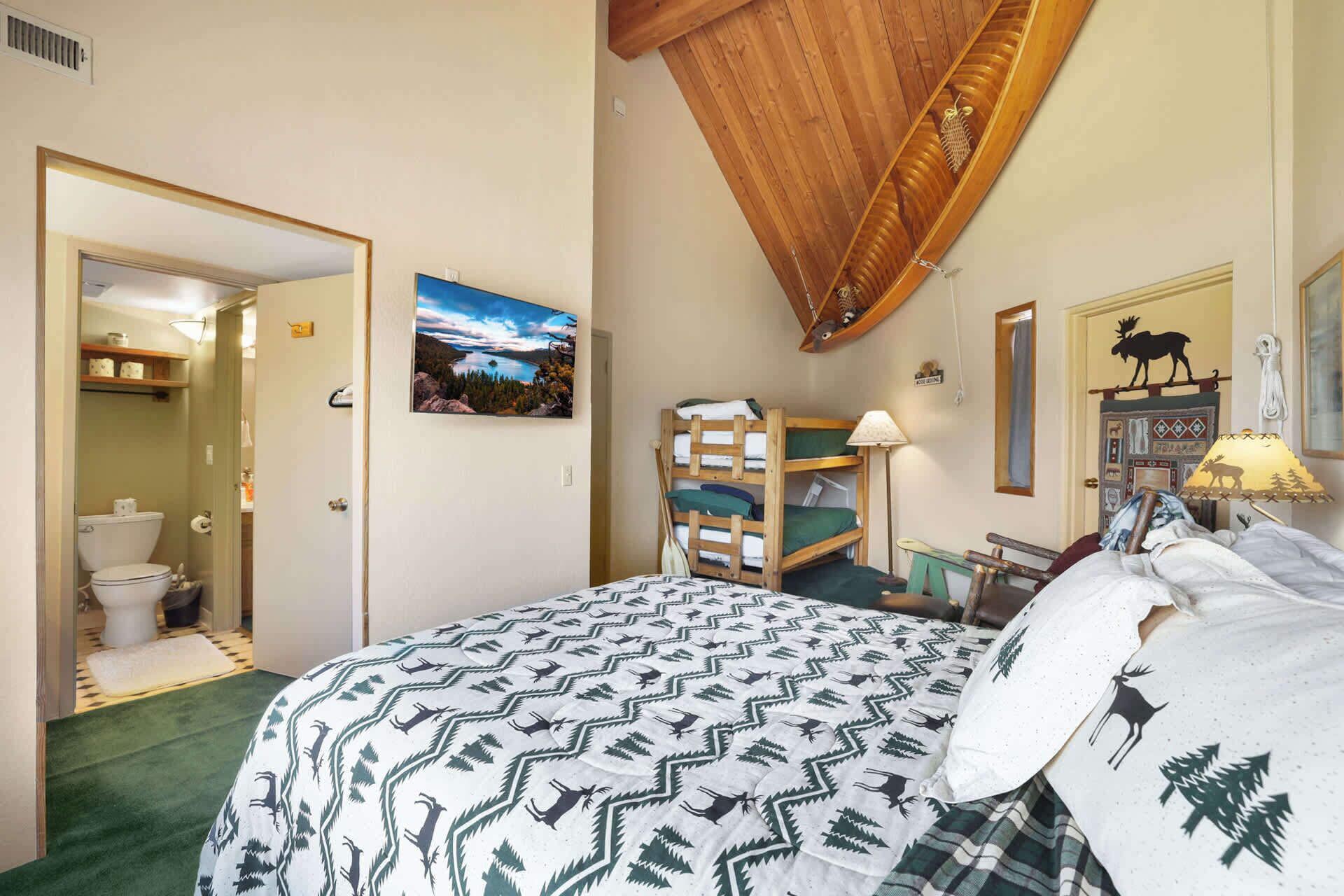 Un dormitorio con una cama litera, un cuadro de un paisaje, una decoración de alce y un techo de madera.