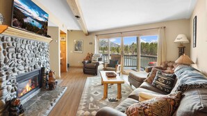 A cozy living room with a stone fireplace, comfortable seating, and a large window offering a scenic view. - Tahoe Keys Marina View: Tahoe Keys short term rental (South Lake Tahoe)