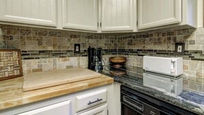 Une cuisine avec des meubles blancs, un pare-feu en pierre, une planche à découper en bois, une machine à café, un grille-pain et un lave-vaisselle.