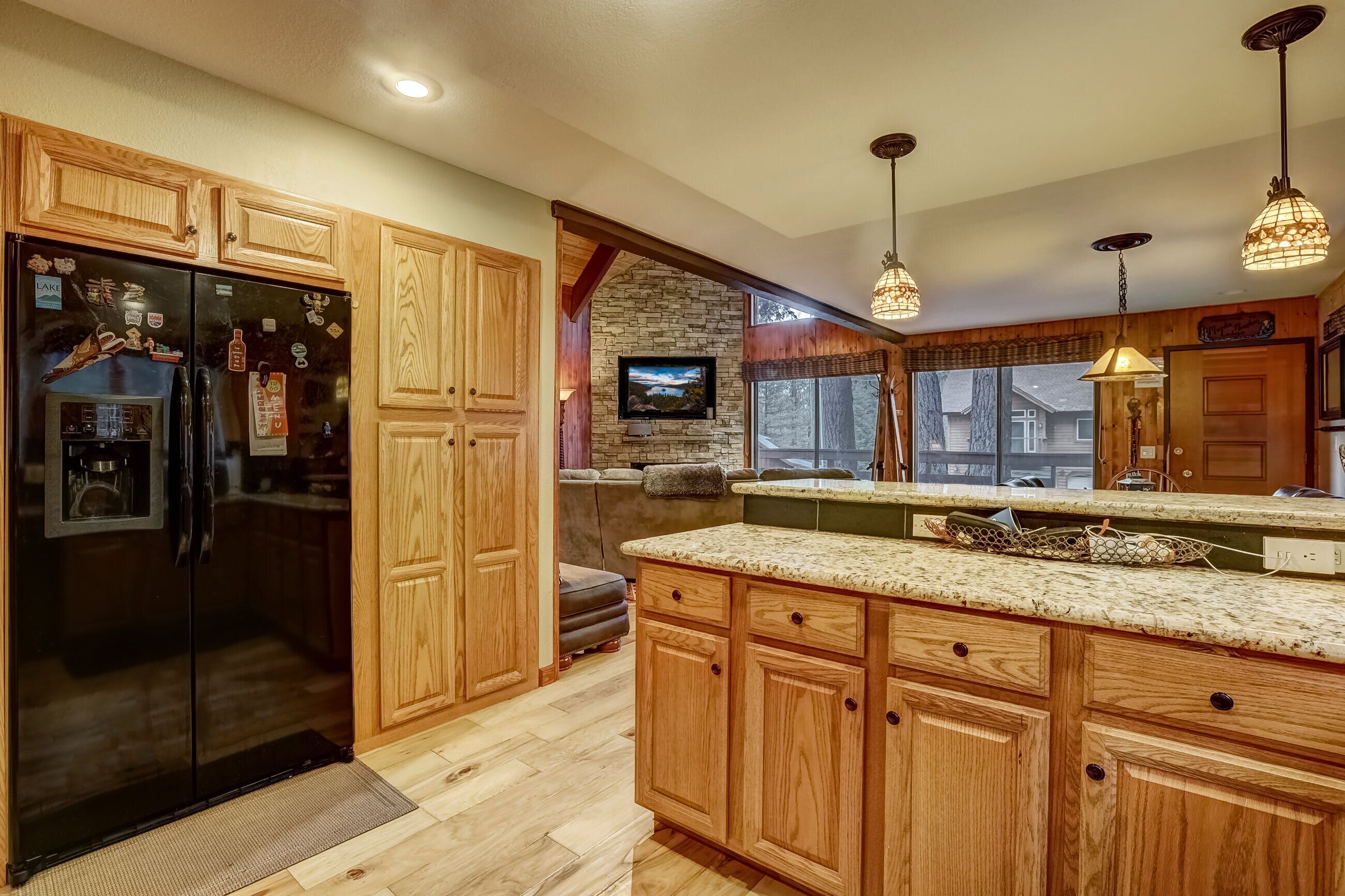 A kitchen with wooden cabinets, a black refrigerator, a stone accent wall, and a large window.