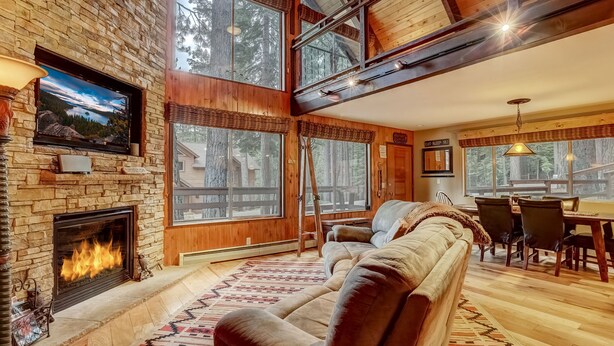 Una sala de estar acogedora con chimenea de piedra, ventanas grandes, un sofá y un comedor.