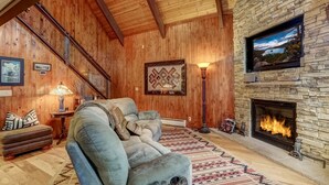 Una sala de estar acogedora con chimenea de piedra, vigas de madera en el techo y un área de estar confortable.