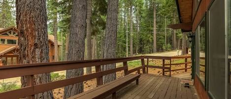A wooden deck with benches, surrounded by tall trees, overlooking a forested area.