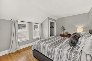 Ein Schlafzimmer mit einem Bett, einem Nachttisch, einer Lampe und einem Fenster mit Vorhängen.