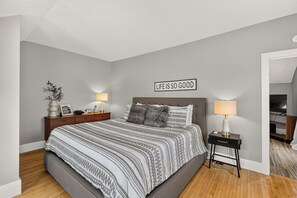 A bedroom with a bed, bedside tables, a nightstand, a wall sign, and a lamp.