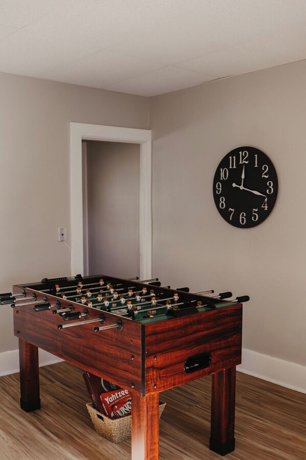 Una habitación con una mesa de futbolín de madera y un reloj de pared.