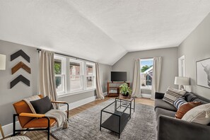 A spacious living room with a sofa, armchair, coffee table, and a TV stand.