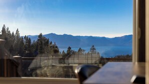 A view from a window overlooking a mountainous landscape with a lake and trees.