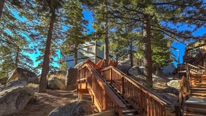 A wooden staircase leading up to a building surrounded by large rocks and pine trees.