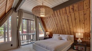 Een slaapkamer met een groot bed, houten wanden, een hanglamp, een boekenplank en uitzicht door een glazen deur.