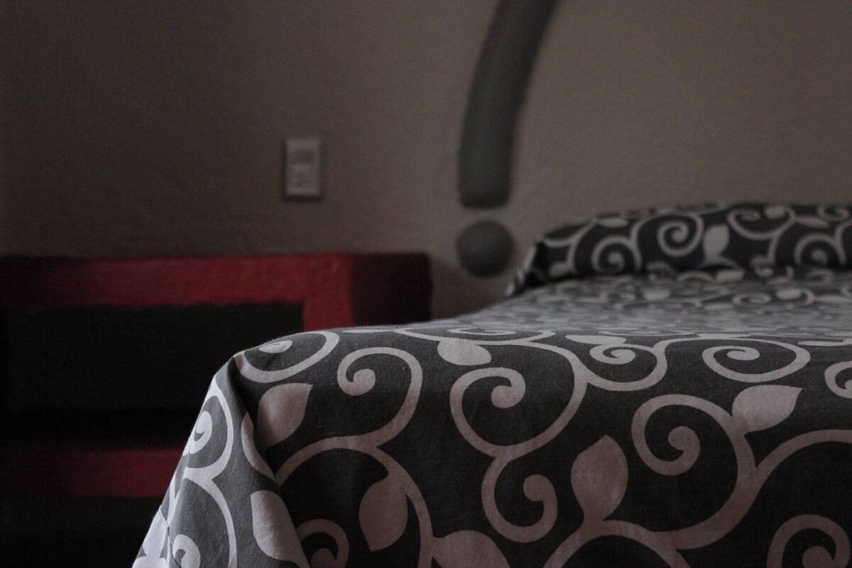 A bed with a black and white patterned bedspread, a red headboard, and a wall with a circular light fixture.