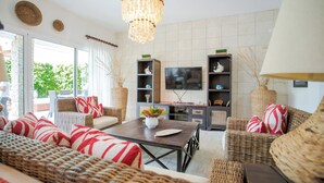 Een moderne woonkamer met rieten meubels, een centrale salontafel en een grote kroonluchter.