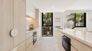 Une cuisine moderne avec des meubles de couleur bois clair, un îlot central, un four encastré et une grande fenêtre donnant sur un paysage verdoyant.