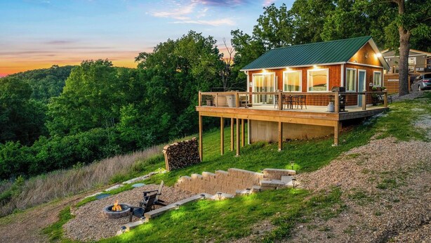 A cabin with a deck, a fire pit, and a view of the surrounding forest. - Views! Private Hot tub and Fire Pit! Lux Couple's Retreat (Omaha)