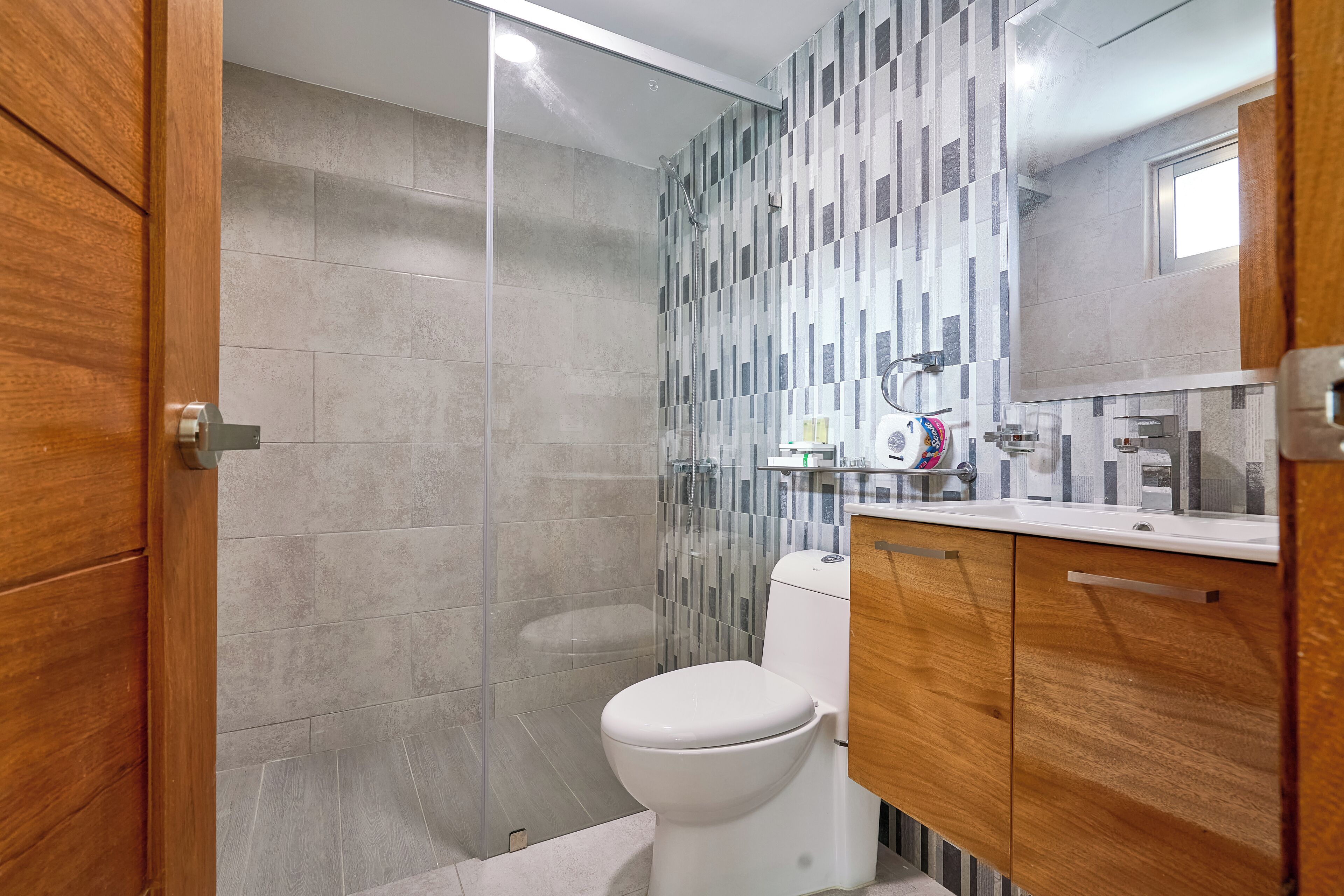 Une salle de bain moderne avec une douche à parois de verre, des toilettes blanches et des meubles en bois.
