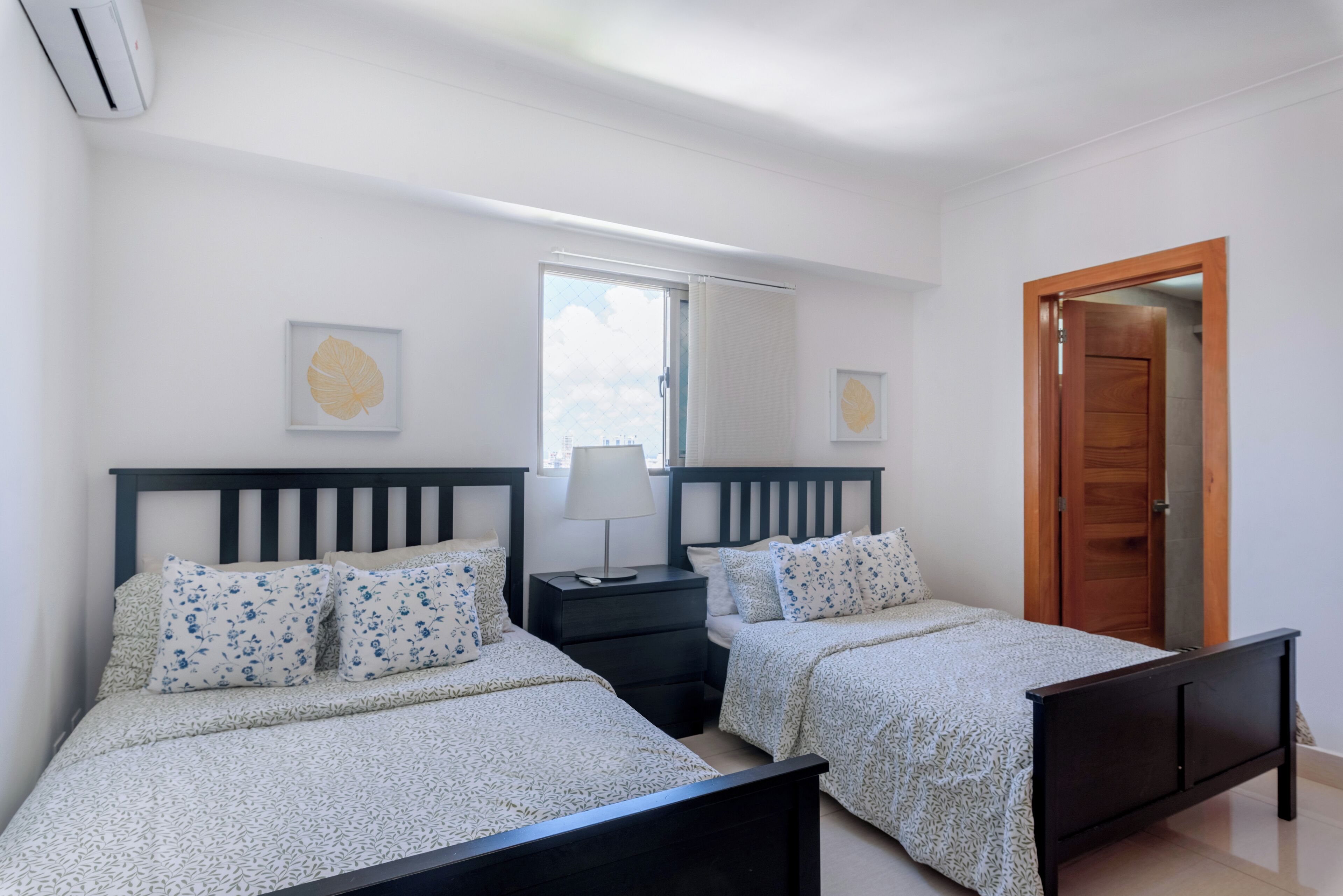 A bedroom with two beds, a nightstand, a mirror, and a wooden door.