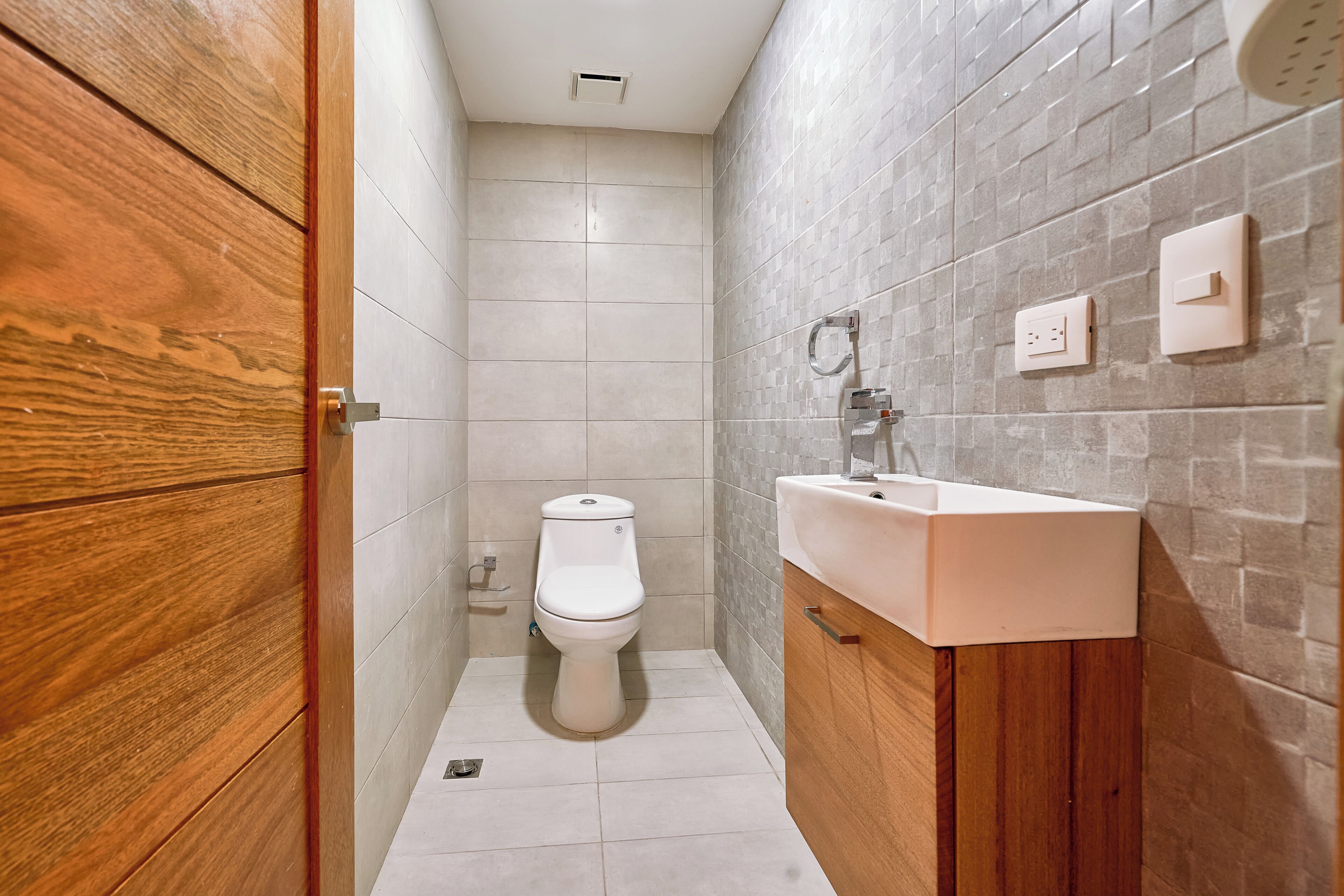 A modern bathroom with a wooden vanity, a white toilet, and a tiled shower area.
