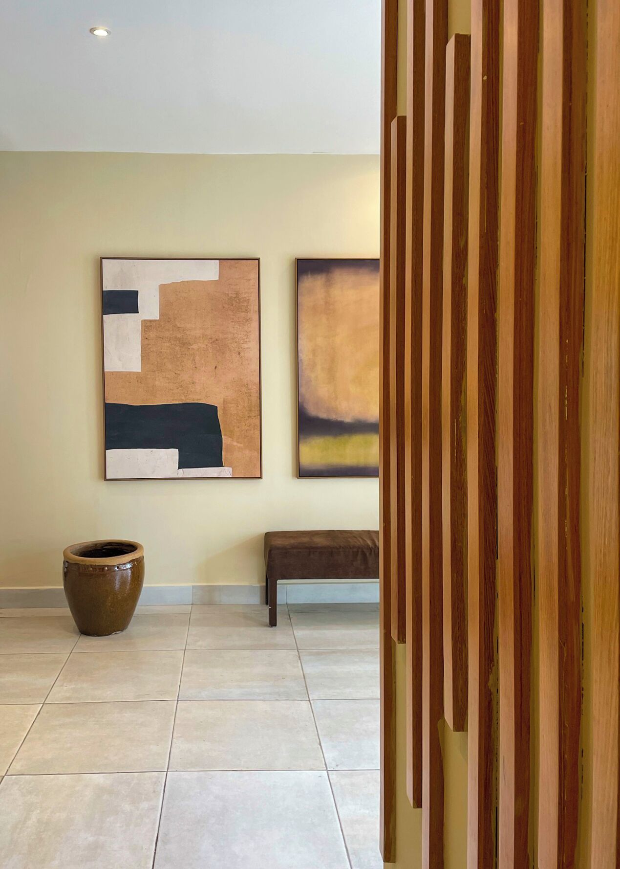 A modern interior with two abstract paintings on the wall, a large ceramic pot, and a bench.