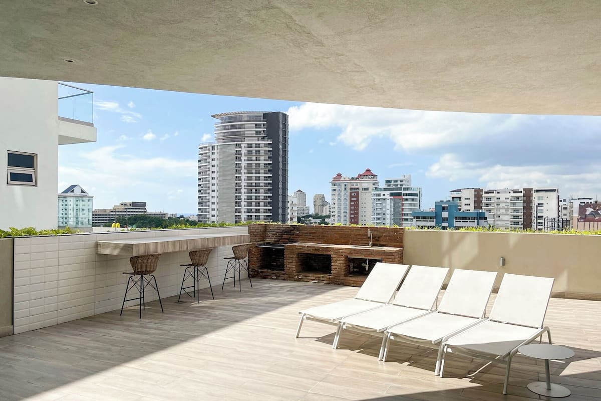 Eine Dachterrasse mit Barbereich, Liegestühlen und einem Kamin aus Ziegeln.