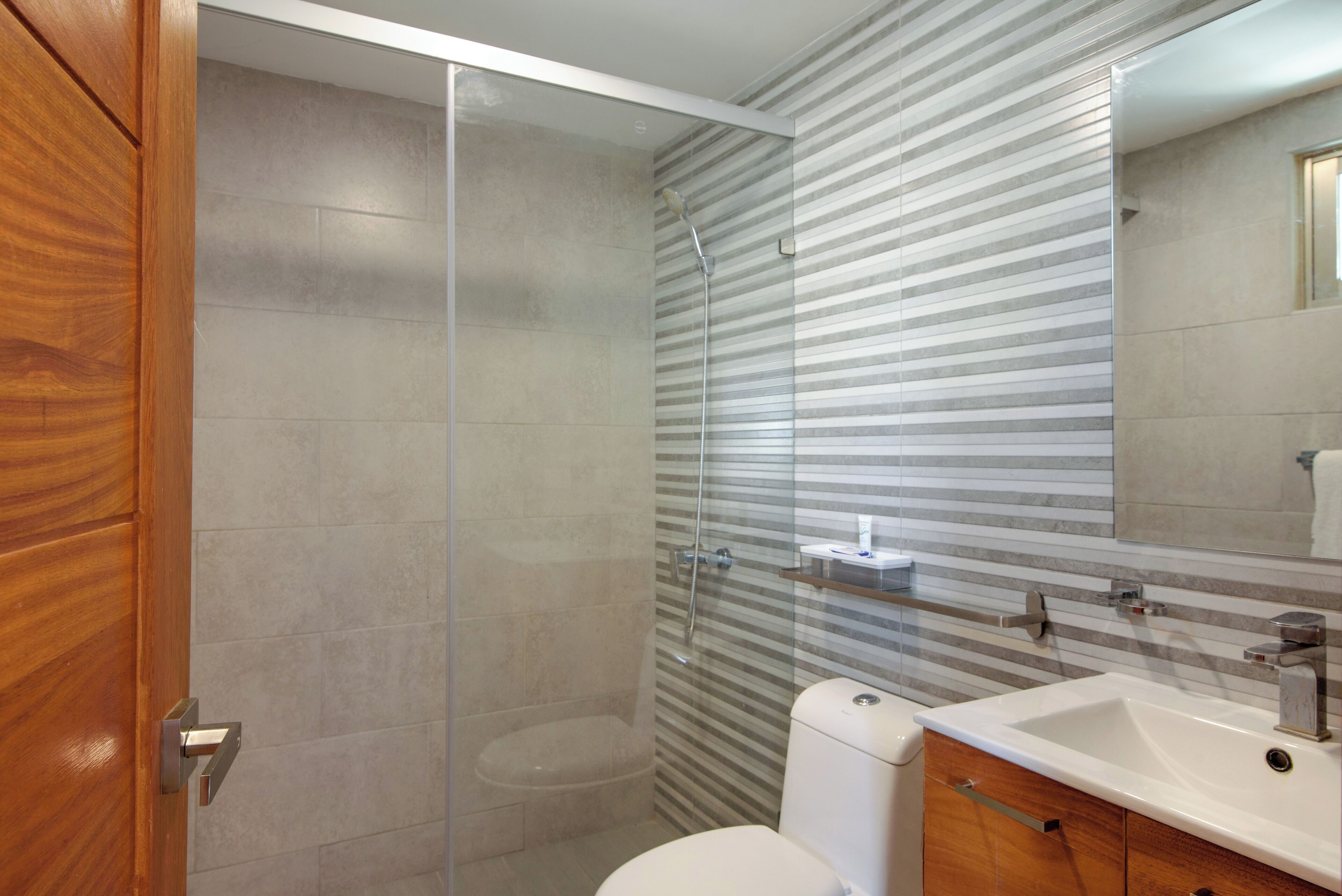 Une salle de bain moderne avec une douche à parois de verre, des toilettes blanches et un meuble-lavabo en bois avec un évier.