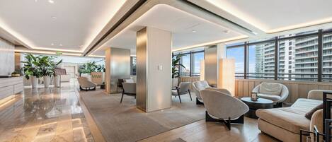 A spacious lobby with a modern design, featuring a reception desk, seating area, and large windows offering views of the city.
