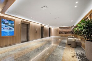 A modern lobby with a marble floor, wooden paneling, a seating area with a spherical decoration, and a wall-mounted advertisement. - AKA Brickell 32th Free Parking by Palermo Home (Miami)