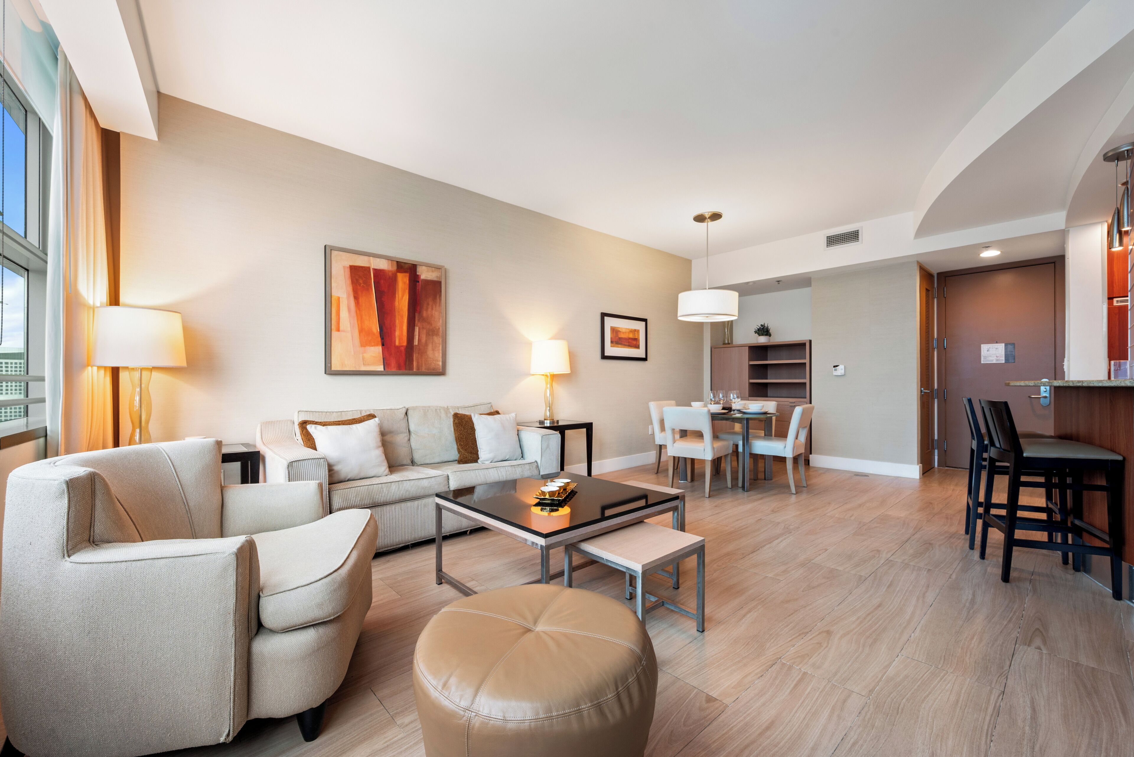 A modern living room with a sofa, ottoman, and dining area with chairs and a table.
