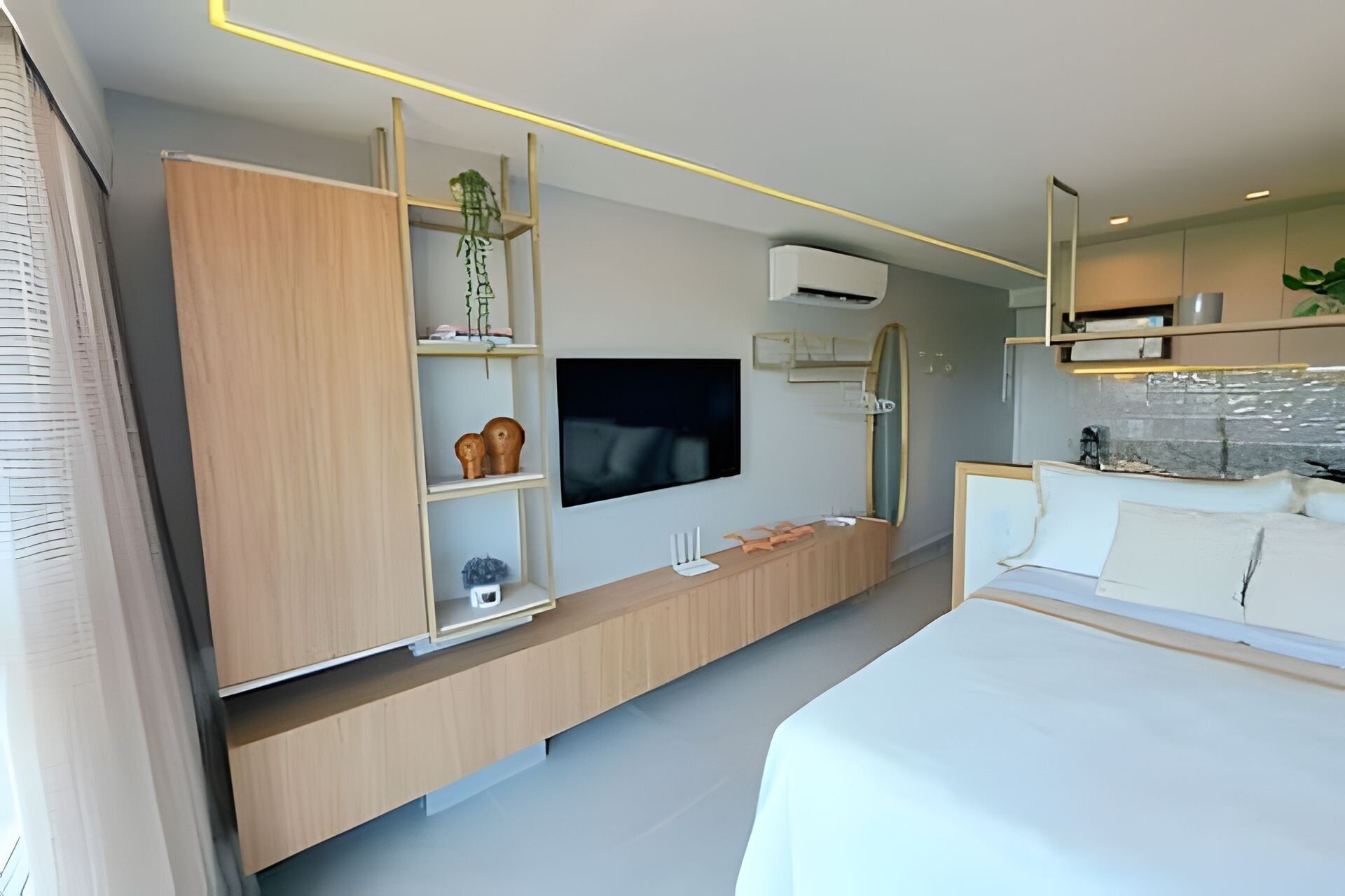 Une chambre moderne comprenant un lit, une télévision, une table de chevet, une armoire et un petit coin cuisine.