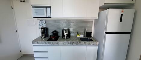 Une cuisine compacte avec des meubles blancs, un four à micro-ondes encastré, une machine à café, un grille-pain et un réfrigérateur.
