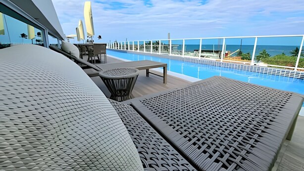 A poolside area with lounge chairs and a table, overlooking a clear blue pool and ocean view. - Ed. Nixxus Residence (Ipojuca)