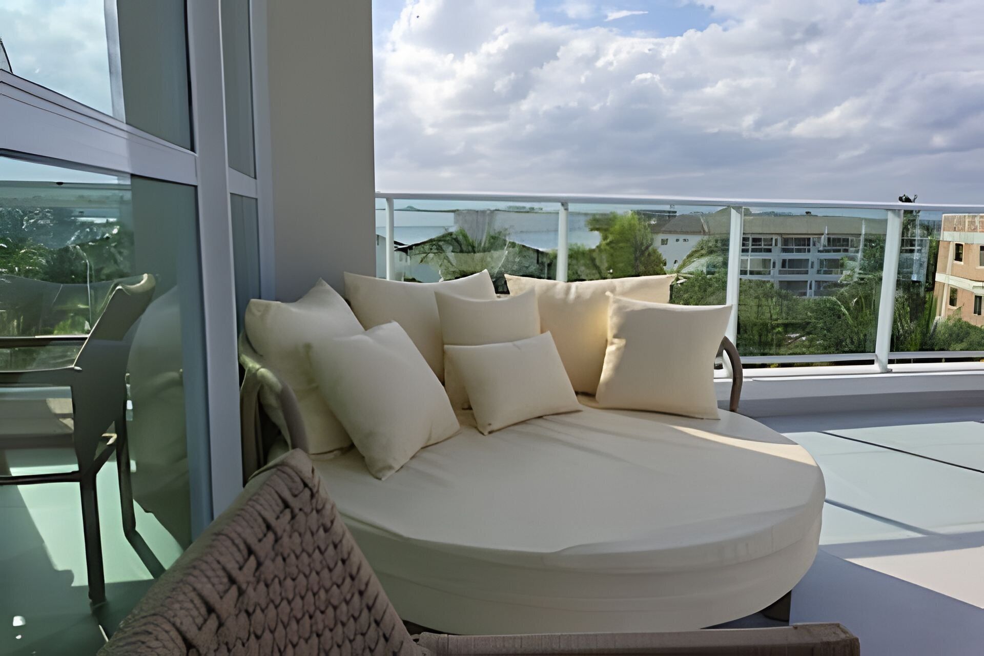 Ein moderner Balkon mit einer gebogenen Couch und Kissen, mit Blick auf eine Stadtlandschaft.