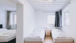 Una habitación con dos camas individuales, una mesita de noche con lámpara, una ventana con cortinas y un radiador.