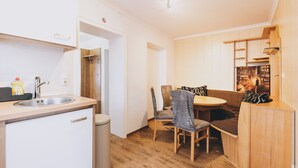 Una cocina compacta con un lavamanos, un refrigerador pequeño y un bote de basura. Hay una zona de comedor con una mesa y sillas de madera.